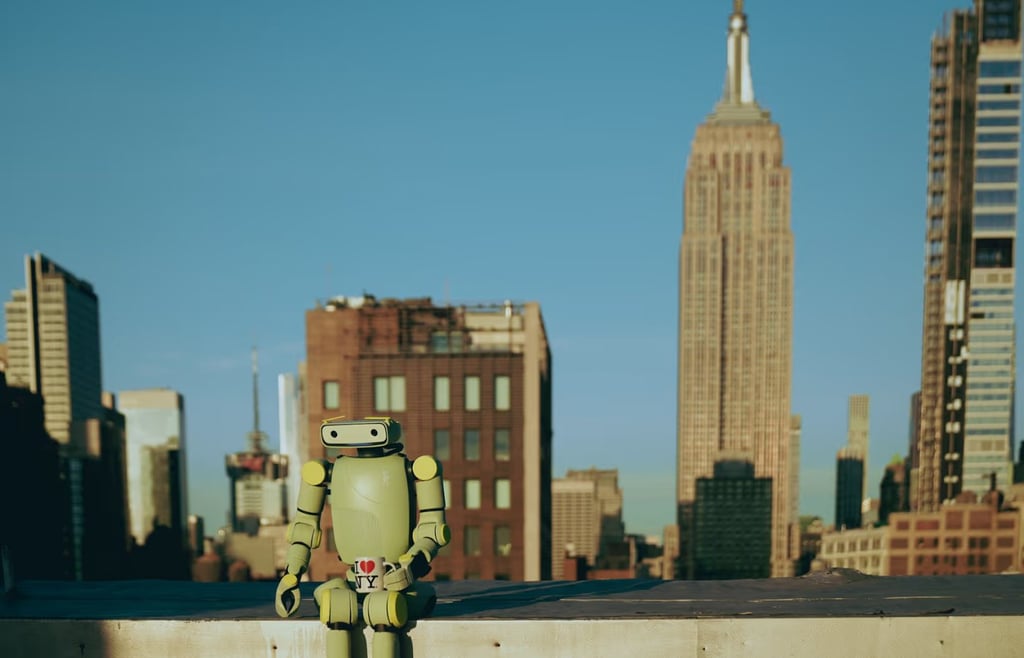A small green vintage-style robot sitting on a rooftop ledge in New York City, holding an 'I Love NY' souvenir mug with the Empire State Building in the background.