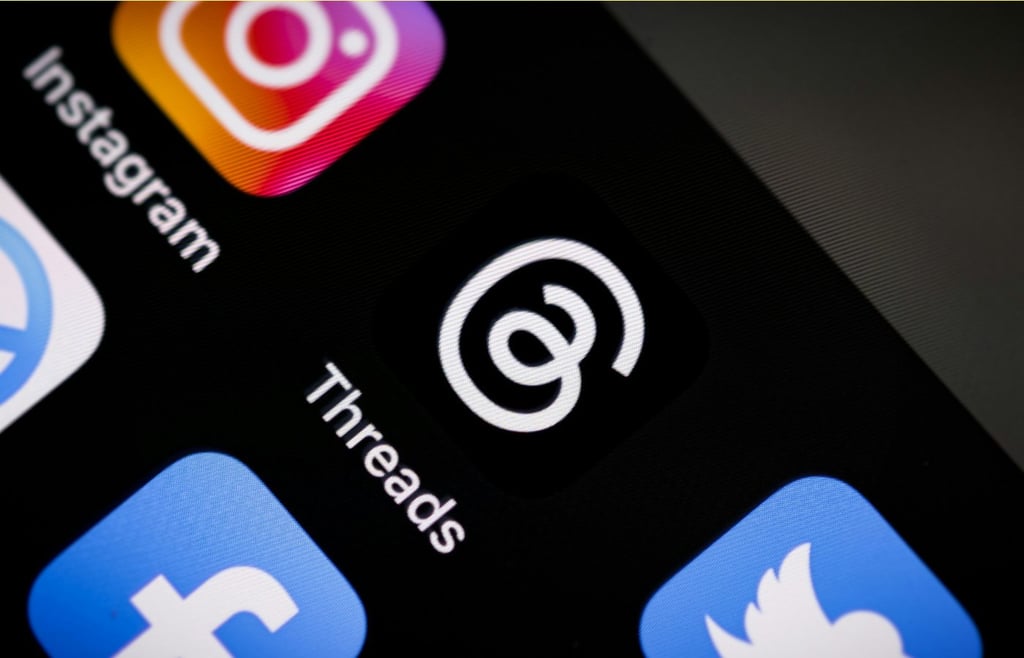 A close-up shot of a smartphone screen showing the Threads app icon prominently next to Instagram, Facebook, and Twitter (X) icons.