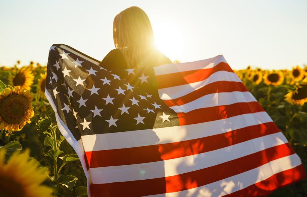 Girl with the US flag on a field of sunflowers.