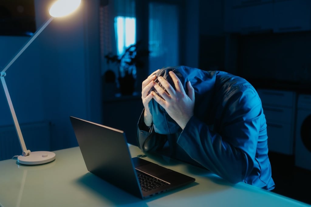 A man depressed while sitting in front of his laptop inside a dark room.