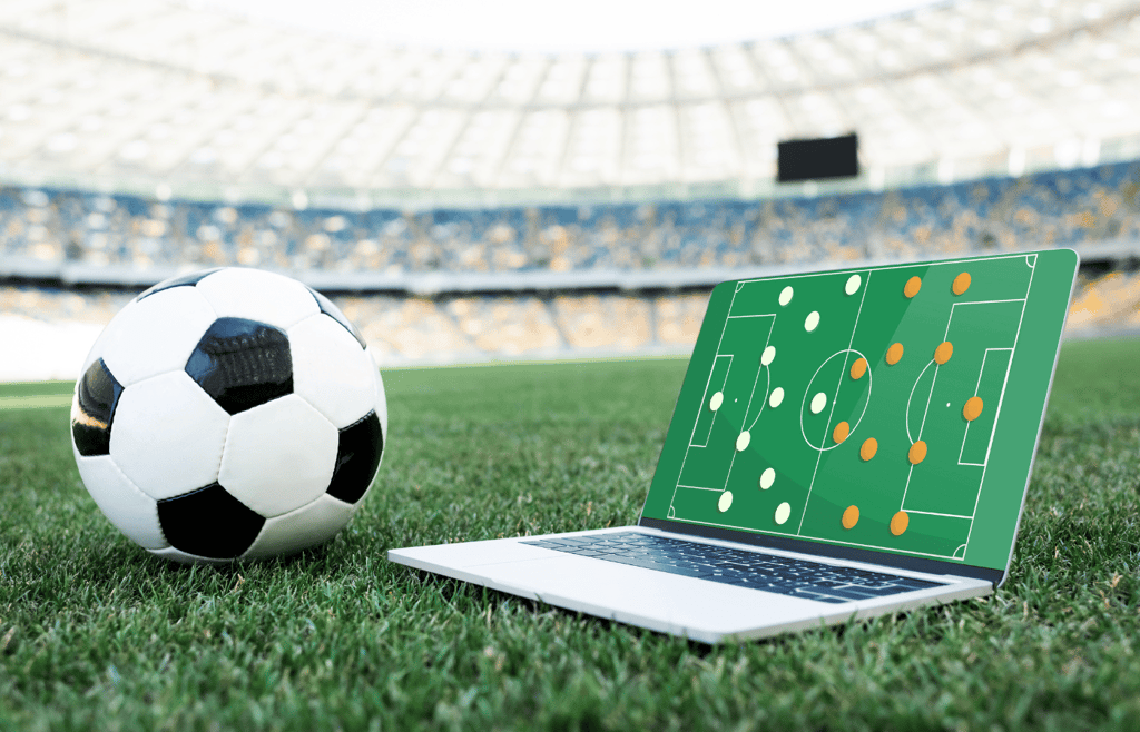 soccer ball and laptop with formation on screen on grassy football pitch at stadium