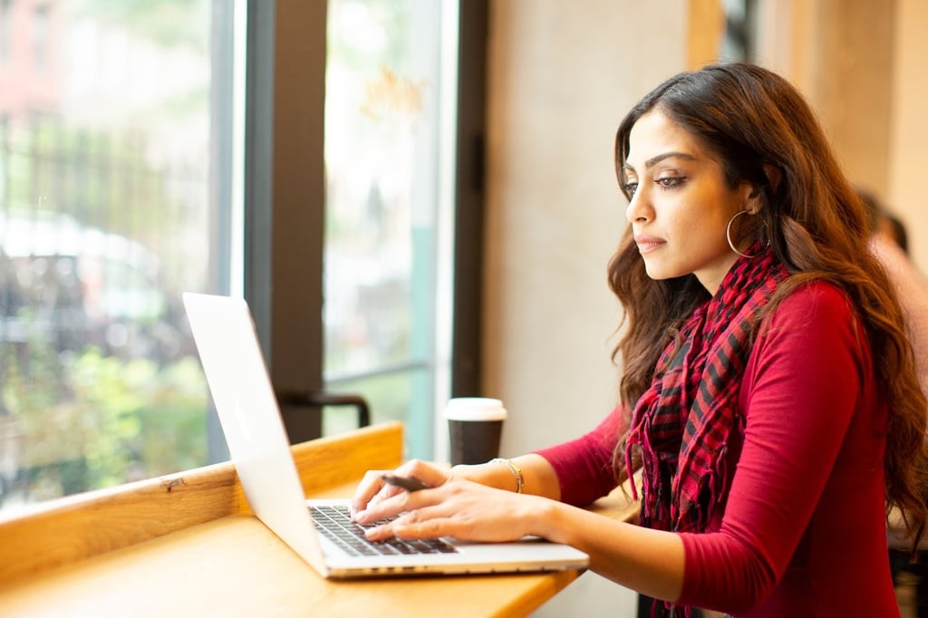woman working on a laptop at a cafe with a coffee cup
