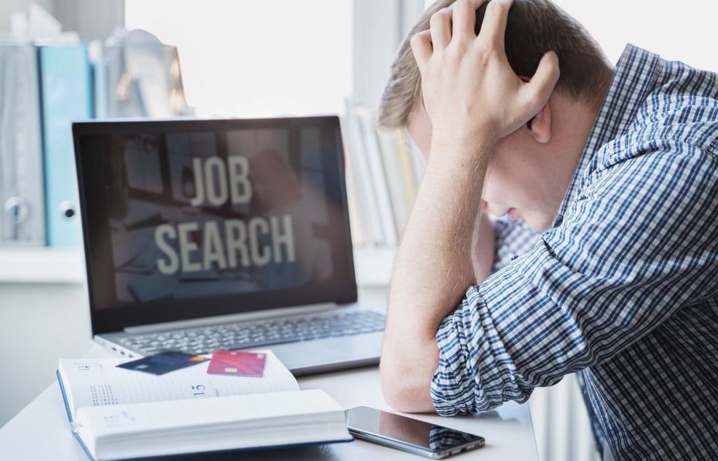 Man holds head with hands on table with laptop. Looking for remote work.
