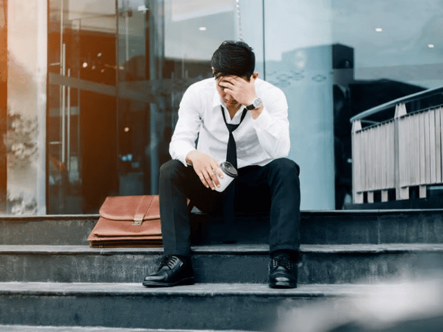 A sad man siting outside the building after he got fired from work.