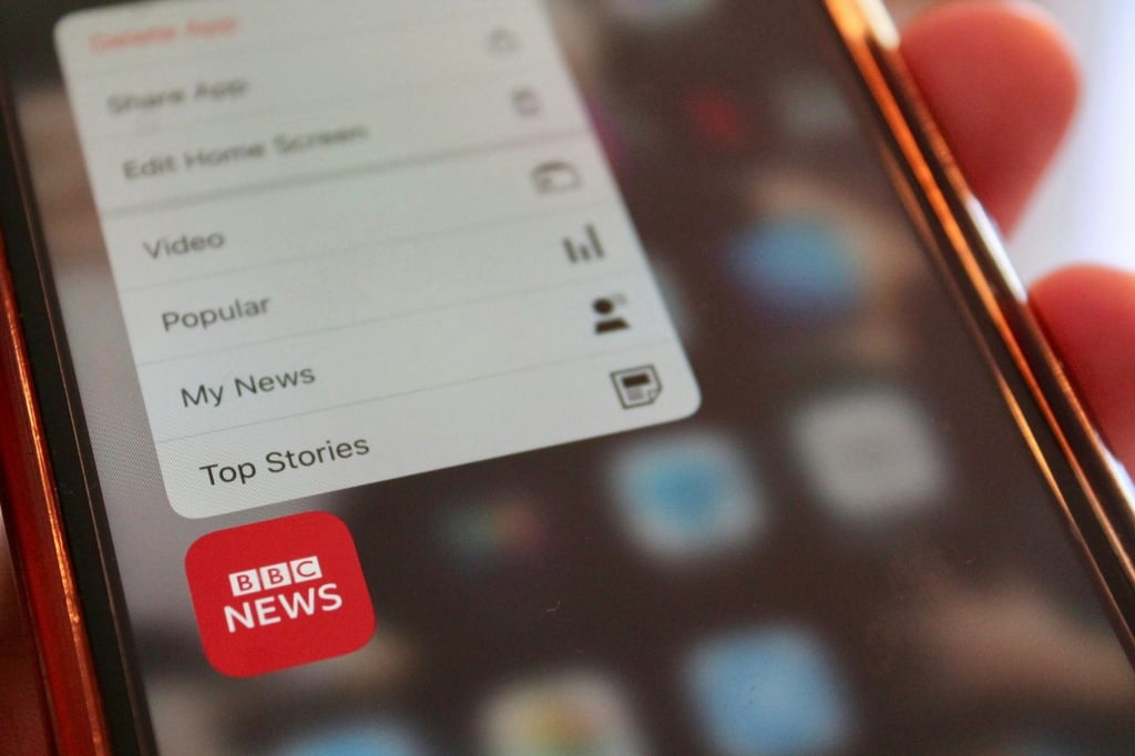 A close up of a person holding a cell phone with the BBC News app.