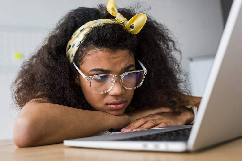 selective focus of upset african american woman in glasses using laptop