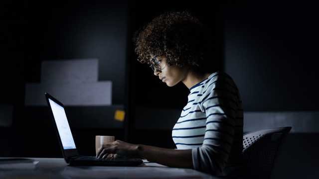 A woman working on her laptop inside a dark room.