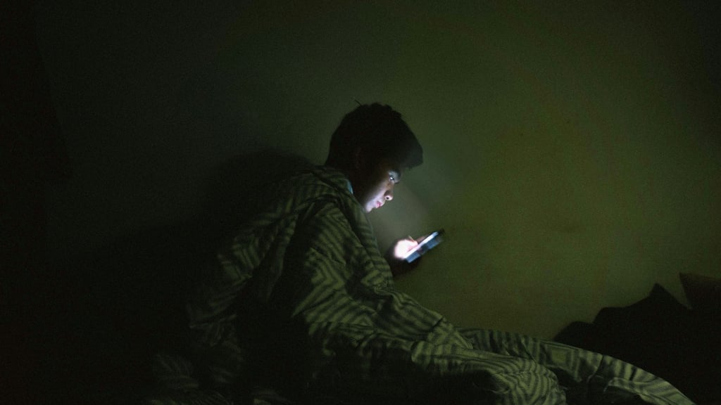 A kid watching on his phone inside a dark bedroom.