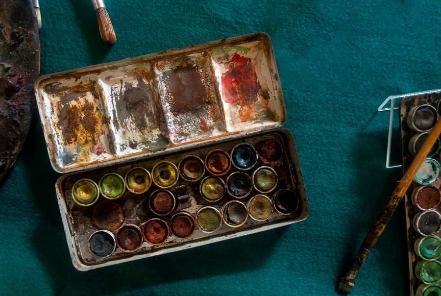 Palette of old mixed paints with a brush lies on an old green cloth table.