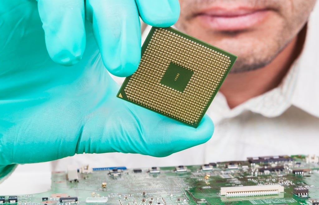 A person holding an processor chip atop a circuit board.