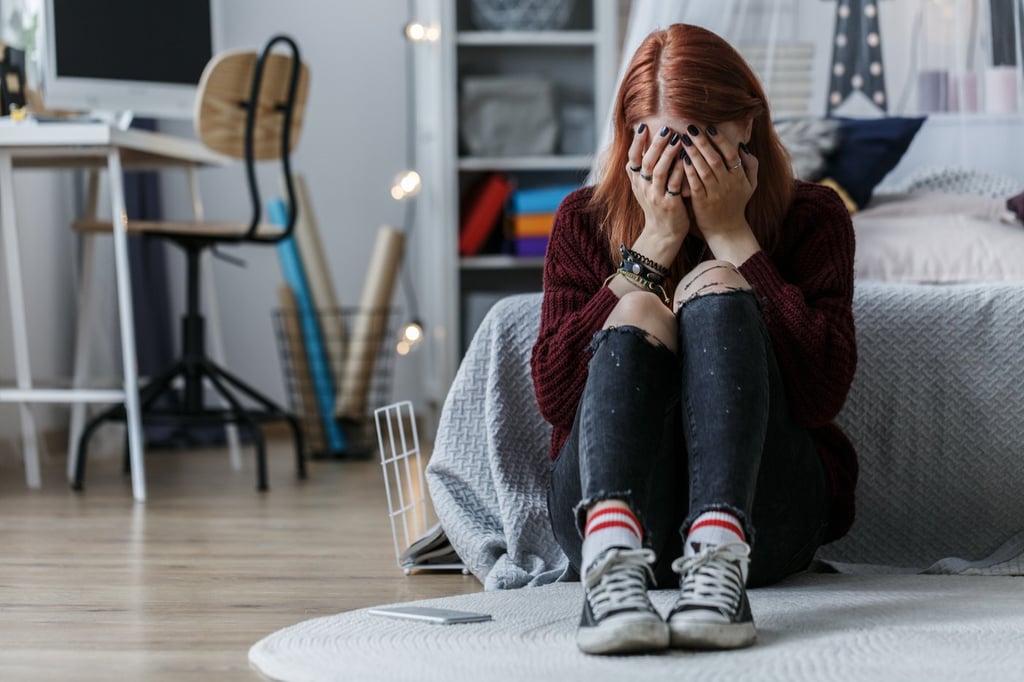 Teenage girl sitting on the floor and crying because of problems at home with parents