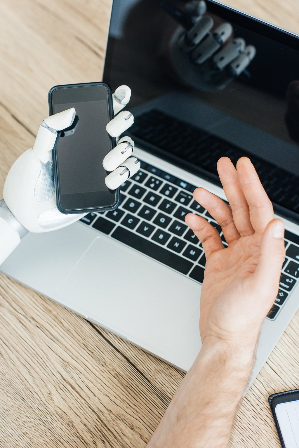 close-up view of human and robot hands using smartphone and laptop at wooden table