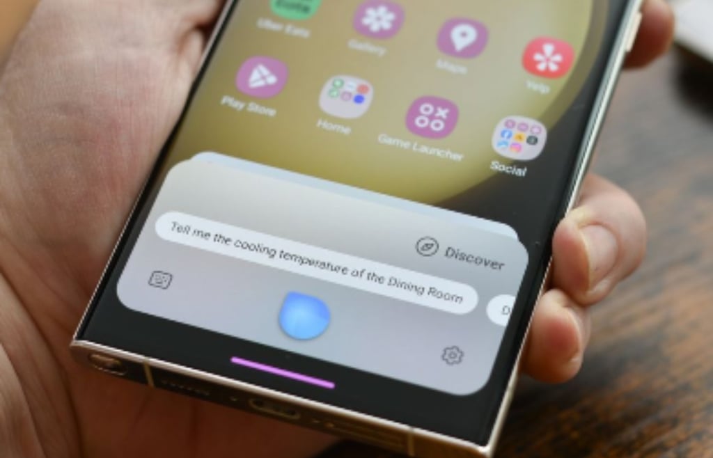 Hand holding a Samsung Galaxy S25 featuring the AI-powered Bixby assistant responding to a complex voice command about home cooling temperatures.