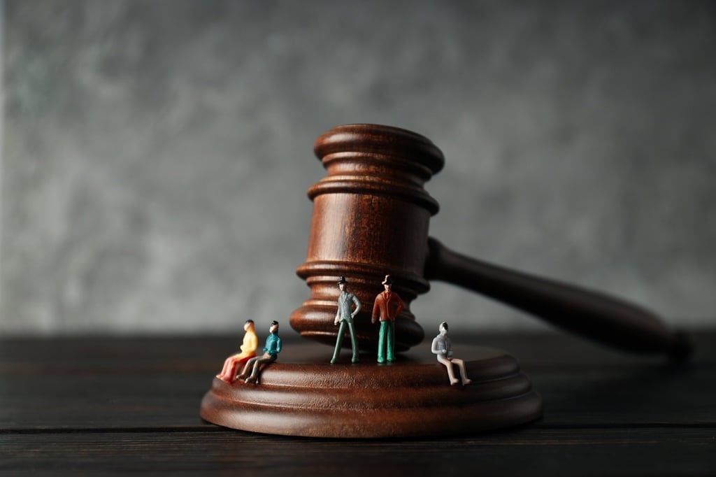 Miniature figures of people stand and sit on the base of a large wooden judge's gavel.