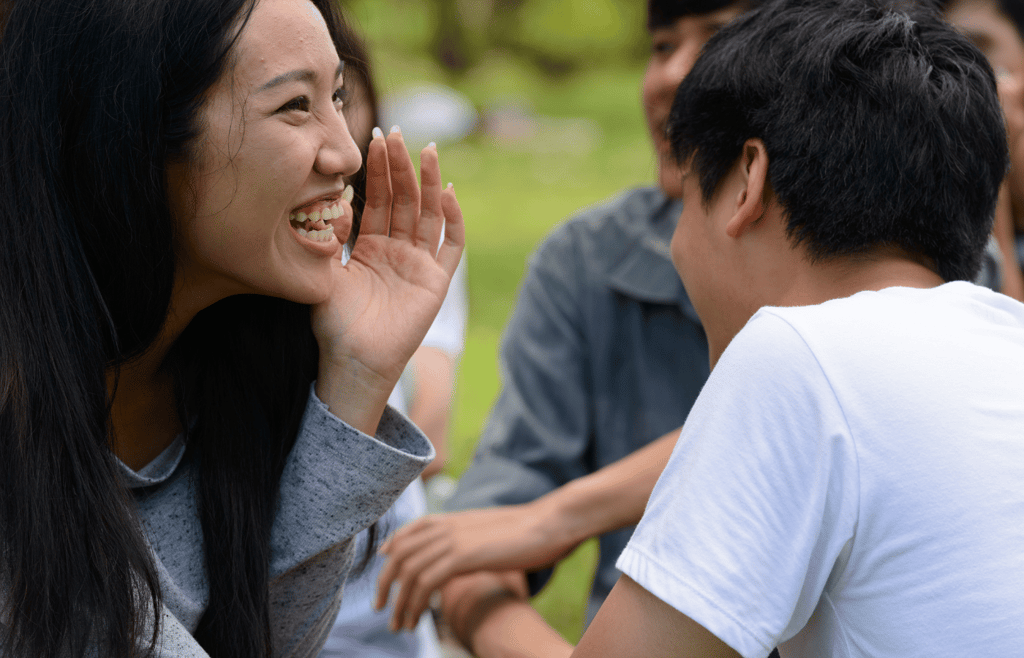 Two young Asian friends whispering together at the park.