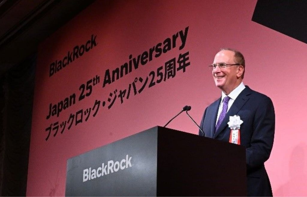 BlackRock CEO Larry Fink speaking at a podium during the BlackRock Japan 25th Anniversary event, with a large red commemorative backdrop.