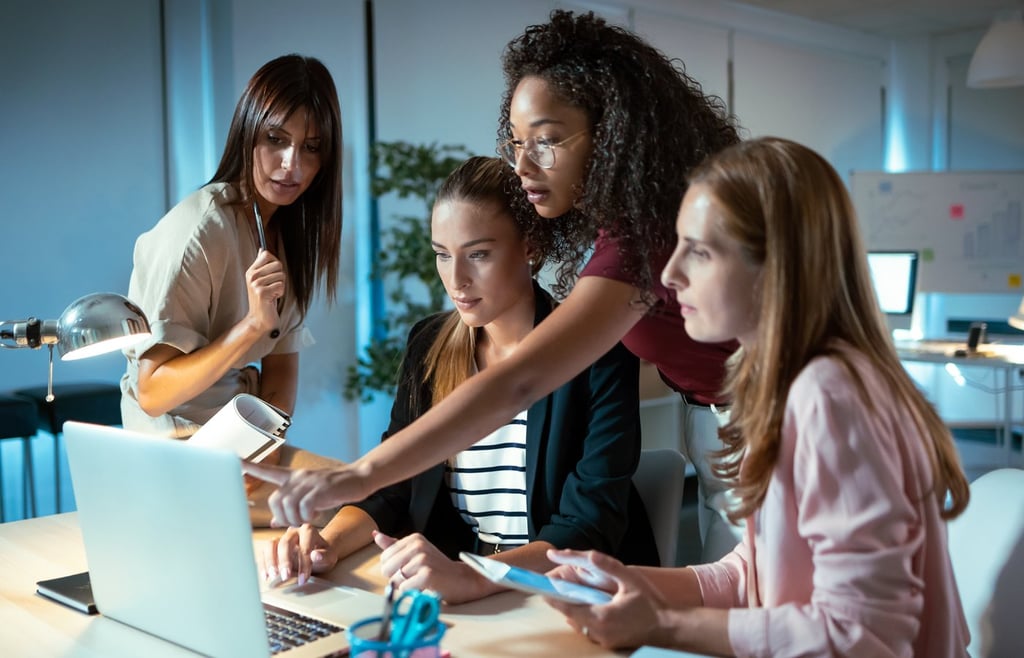Four businesswomen talking and reviewing the latest work done on the computer in a joint workspace.