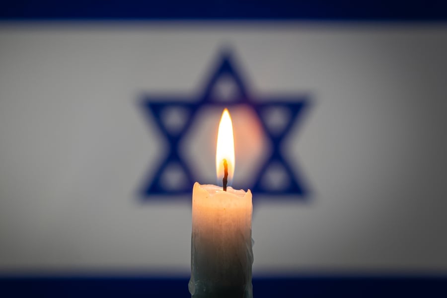 This stock photo from Adobe Stock features a lit candle with the Israel flag in the background.