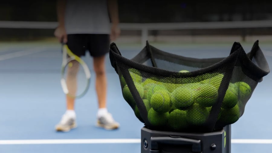 A man playing tennis with an AI assistant throwing tennis balls.
