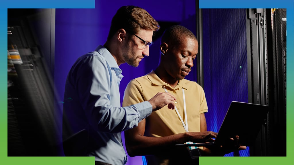 Two coworkers in an industrial environment look at a laptop together