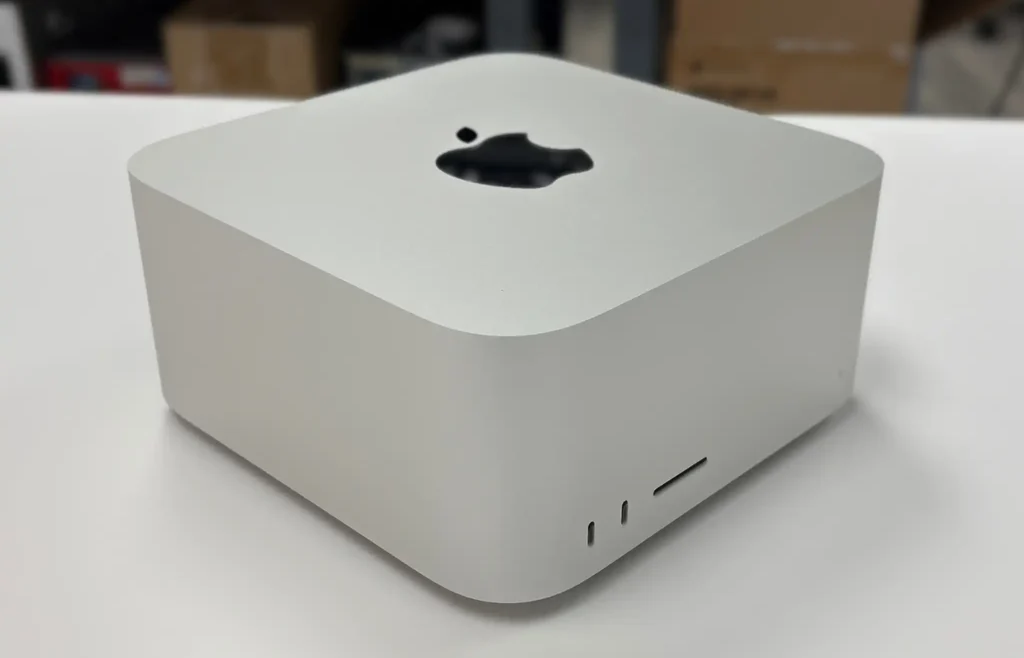 An Apple Mac Studio desktop computer sitting on a white table showcasing the front ports and top logo.