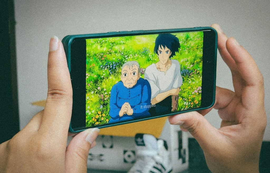 A person holding up a cell phone watching anime