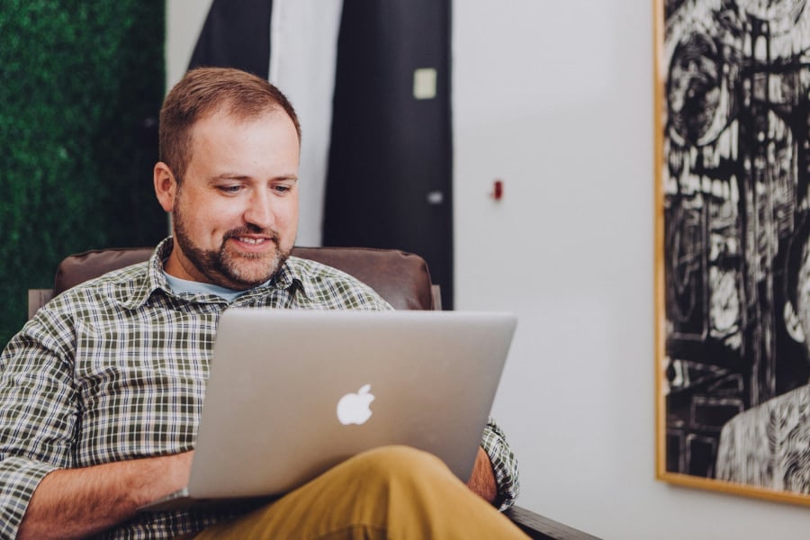 A mn sitting on a chair while on his laptop.