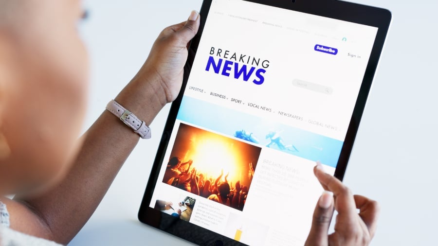 A woman holding a tablet with breaking news of current events in the homepage.