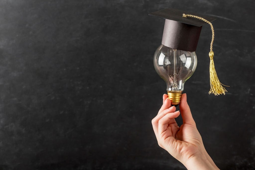 A hand holding a lightbulb with a graduation cap.
