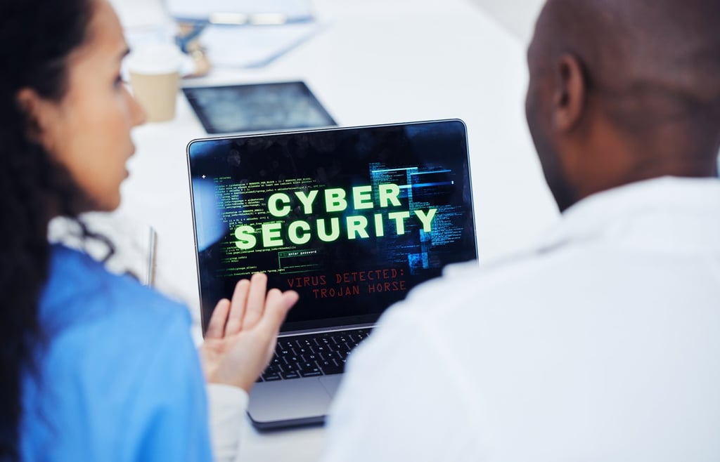 Two IT professionals discussing infront of a laptop with cybersecurity alert warning on display.