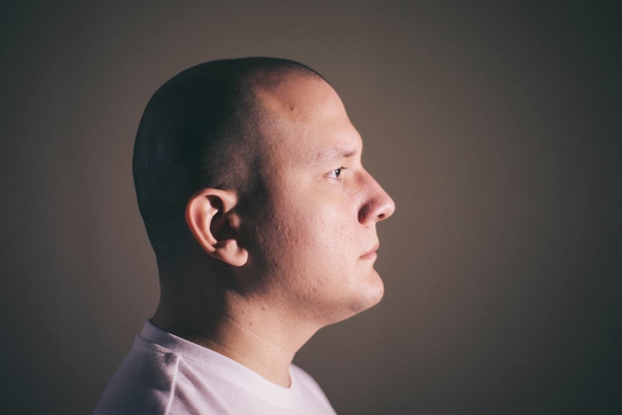 A Bald man in white crew neck shirt facing sideways.