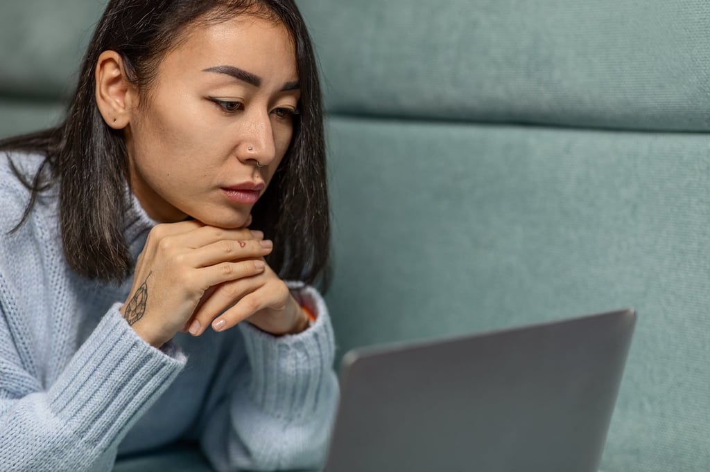 A young woman in a light blue sweater concentrates while working on a laptop computer.