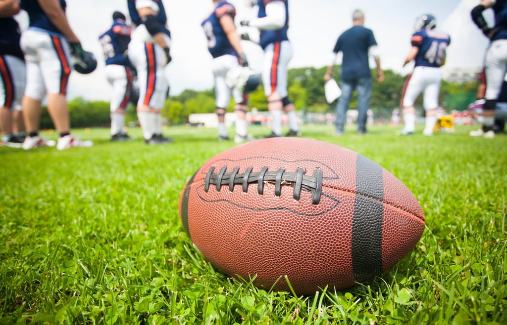 Close up of a football on a field with players on the background.
