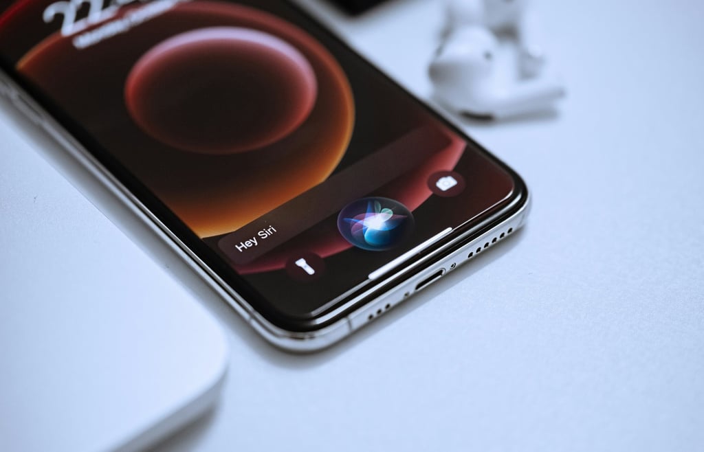 Apple iPhone 12 Pro displaying the Siri interface alongside white AirPods on a desk.