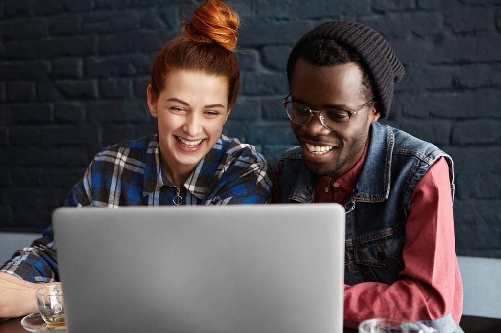 Two friends laughing while in front of laptop.