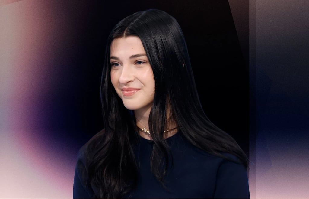 Phoebe Gates smiling during a TV interview, wearing a dark navy top and gold necklace.