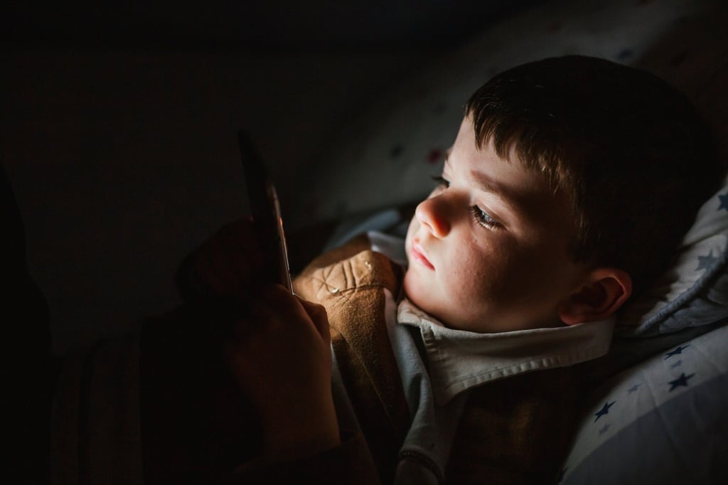 Portrait of little boy lying in bed using smartphone.